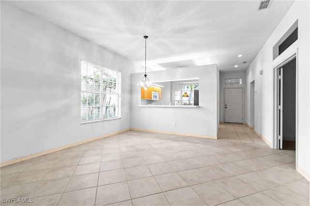 tiled spare room featuring a healthy amount of sunlight and a notable chandelier