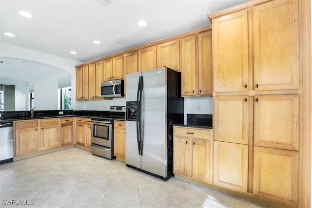 kitchen featuring light brown cabinetry, stainless steel appliances, sink, dark stone countertops, and light tile patterned flooring