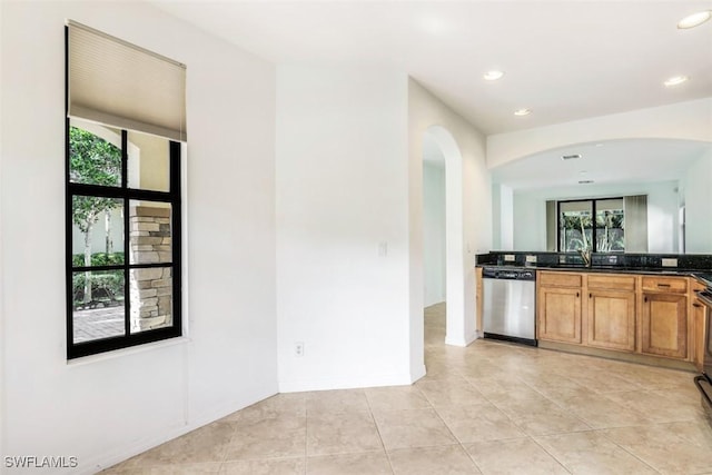 kitchen featuring stove, stainless steel dishwasher, dark stone counters, sink, and light tile patterned floors