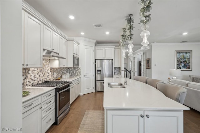 kitchen with appliances with stainless steel finishes, white cabinetry, sink, dark hardwood / wood-style flooring, and a center island with sink