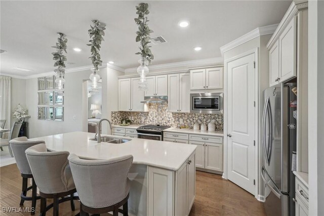 kitchen with an island with sink, appliances with stainless steel finishes, sink, and pendant lighting