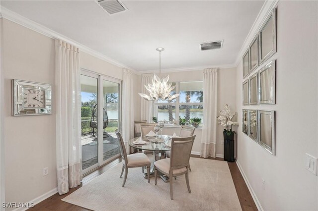 dining space featuring hardwood / wood-style flooring, a water view, ornamental molding, and a chandelier