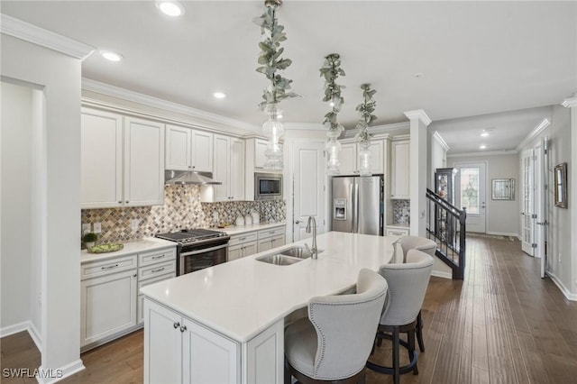 kitchen featuring pendant lighting, sink, appliances with stainless steel finishes, white cabinetry, and a center island with sink