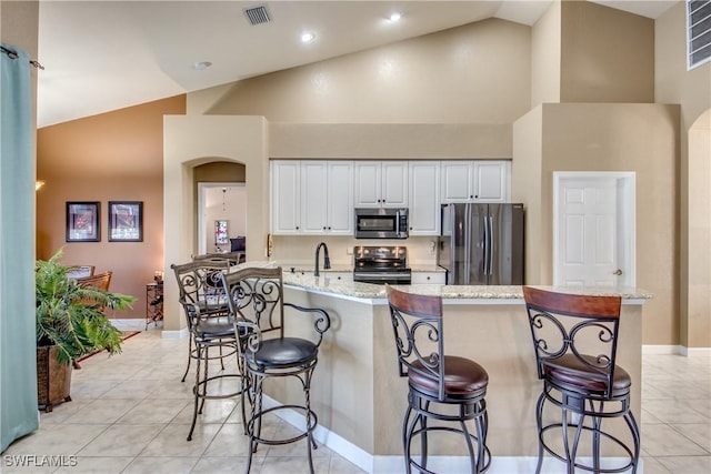 kitchen with high vaulted ceiling, white cabinets, a breakfast bar area, light tile patterned floors, and stainless steel appliances