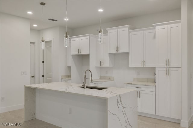 kitchen featuring decorative light fixtures, sink, a kitchen island with sink, and white cabinetry