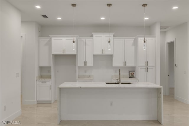 kitchen featuring light stone countertops, a kitchen island with sink, white cabinetry, and hanging light fixtures