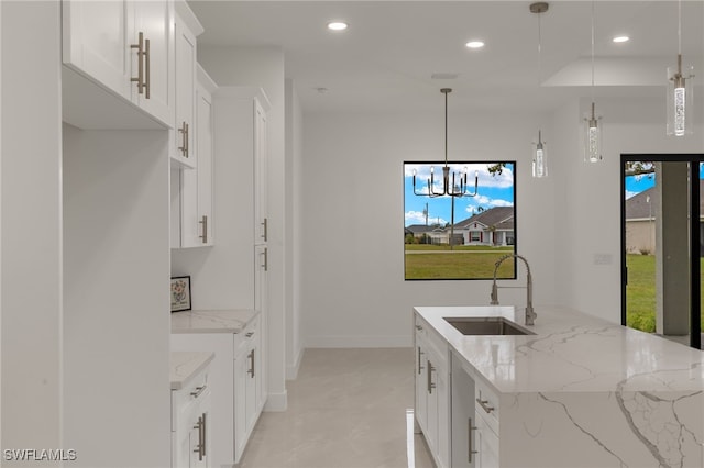 kitchen with sink, white cabinetry, light stone counters, hanging light fixtures, and a kitchen island with sink