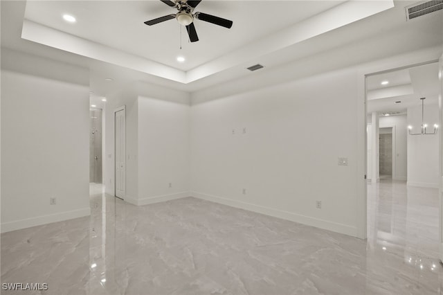 unfurnished room featuring ceiling fan with notable chandelier and a raised ceiling