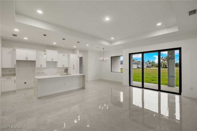 kitchen with decorative light fixtures, white cabinetry, a center island with sink, a chandelier, and a tray ceiling