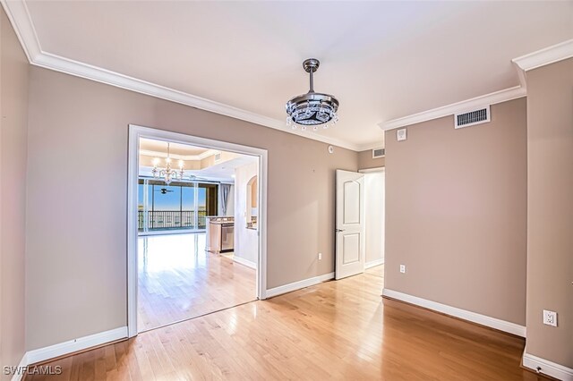 unfurnished room featuring crown molding, an inviting chandelier, light wood-style flooring, baseboards, and visible vents