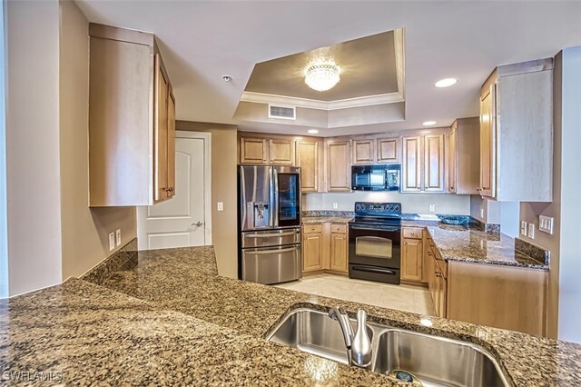 kitchen featuring visible vents, dark stone counters, a tray ceiling, a sink, and black appliances