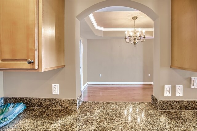 unfurnished dining area with crown molding, arched walkways, a chandelier, and wood finished floors