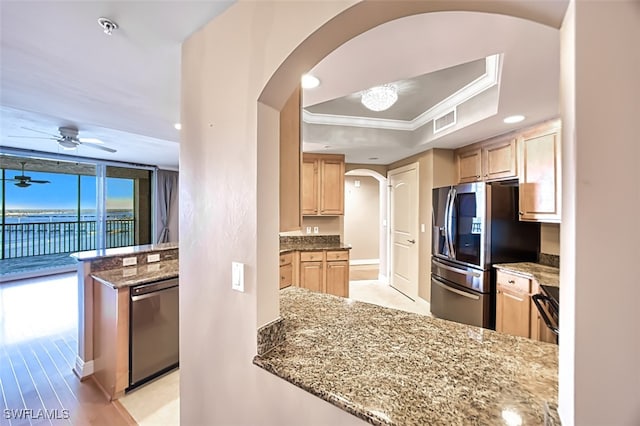 kitchen with appliances with stainless steel finishes, light stone counters, a tray ceiling, crown molding, and light brown cabinets