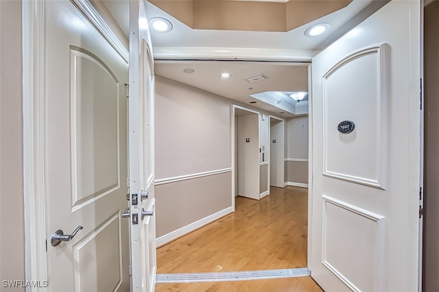 corridor featuring a skylight, recessed lighting, baseboards, and light wood finished floors