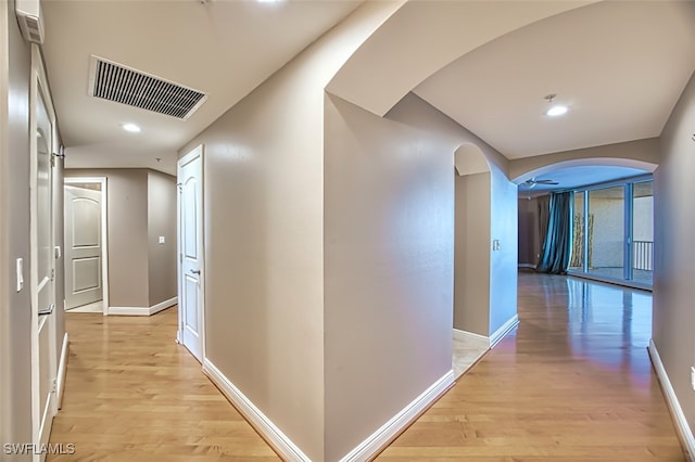 hallway with arched walkways, baseboards, light wood-type flooring, and visible vents