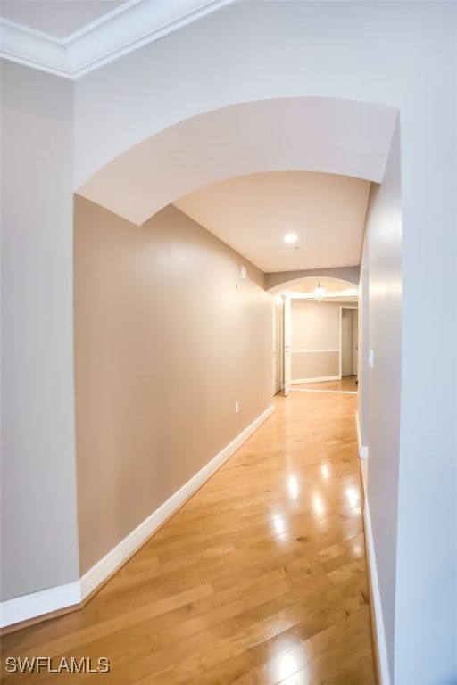 hallway with arched walkways, baseboards, and light wood-style flooring