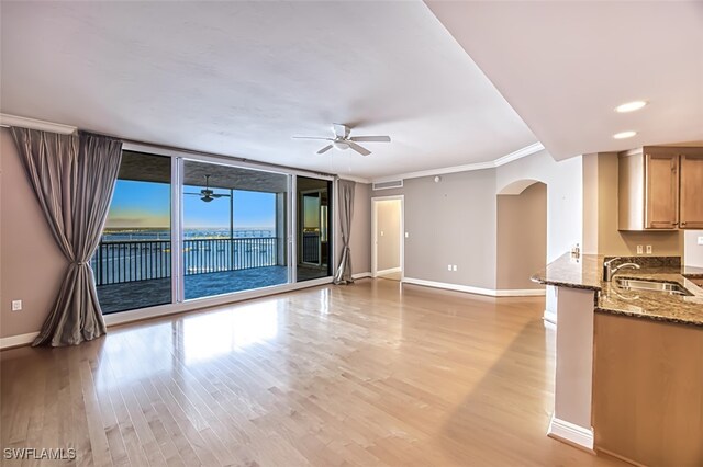 unfurnished living room with a ceiling fan, crown molding, arched walkways, a sink, and baseboards