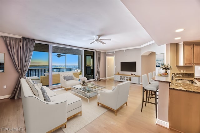 living room with baseboards, ornamental molding, a ceiling fan, and light wood finished floors