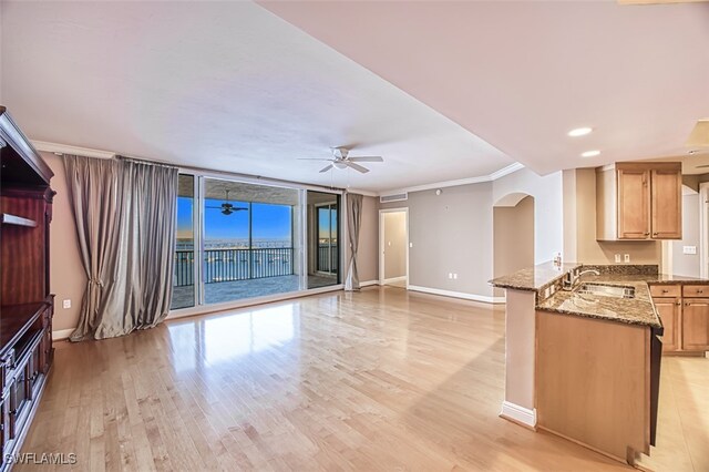 unfurnished living room with a ceiling fan, arched walkways, a sink, baseboards, and light wood-style floors