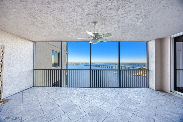 empty room with a water view, a textured ceiling, ceiling fan, and tile patterned flooring