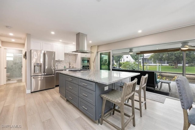 kitchen featuring a kitchen island, decorative backsplash, white cabinetry, appliances with stainless steel finishes, and island range hood