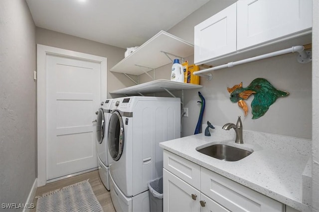 laundry area with light wood-type flooring, cabinets, washer and clothes dryer, and sink