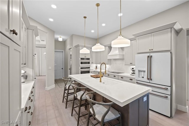 kitchen with premium range hood, a center island with sink, a kitchen breakfast bar, hanging light fixtures, and high end fridge