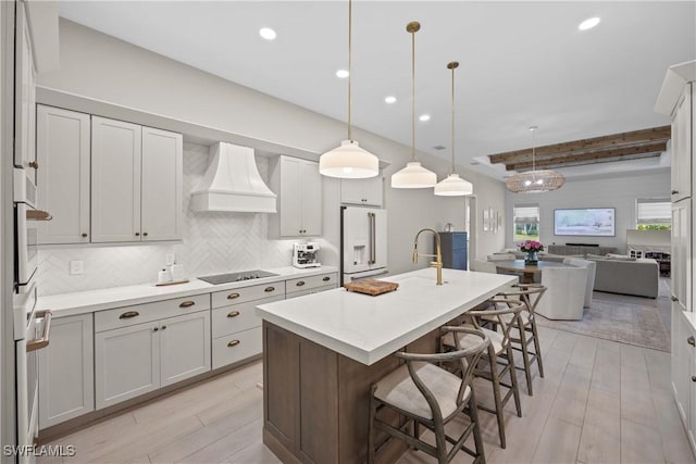 kitchen with hanging light fixtures, a kitchen breakfast bar, white appliances, a center island with sink, and custom exhaust hood