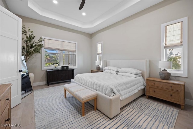 bedroom with ceiling fan, a raised ceiling, and light hardwood / wood-style flooring