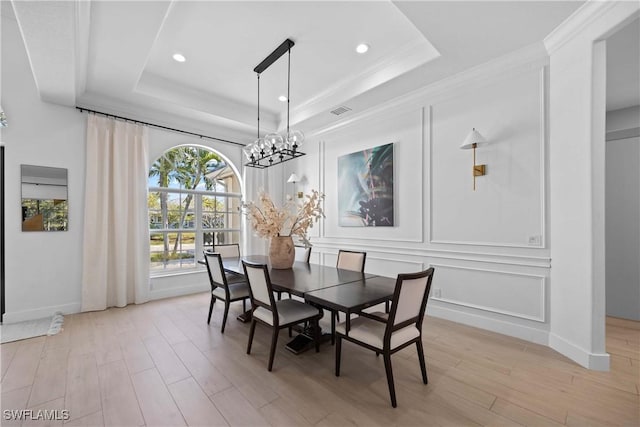 dining area with a tray ceiling, crown molding, light hardwood / wood-style floors, and an inviting chandelier