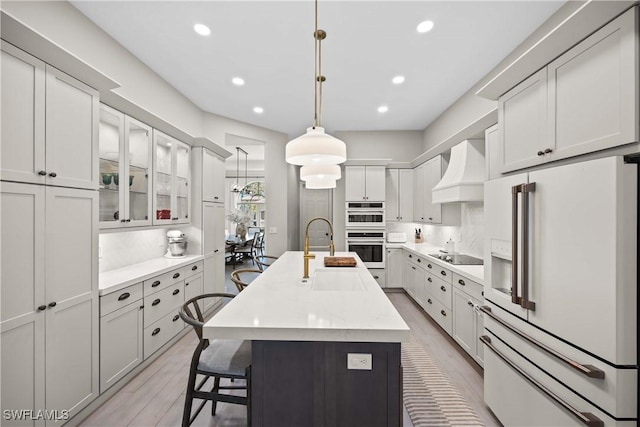 kitchen featuring sink, pendant lighting, high end white refrigerator, a center island with sink, and custom exhaust hood