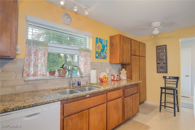 kitchen featuring sink, ceiling fan, white dishwasher, backsplash, and light stone countertops