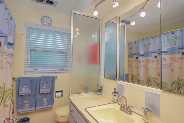 bathroom with toilet, vanity, and tile walls