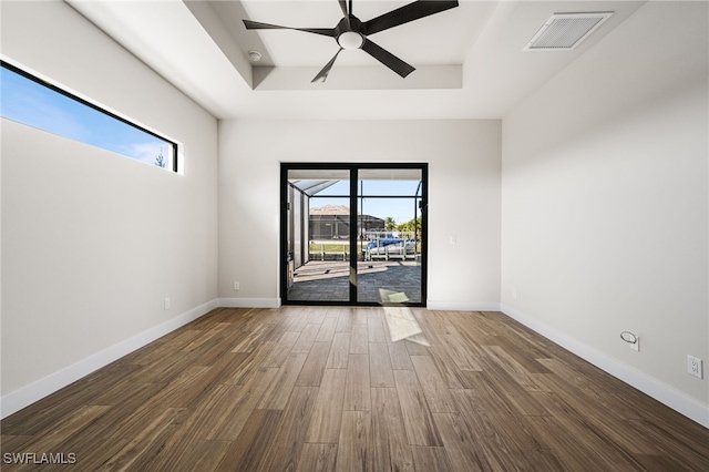 spare room with ceiling fan, dark hardwood / wood-style floors, a raised ceiling, and a healthy amount of sunlight