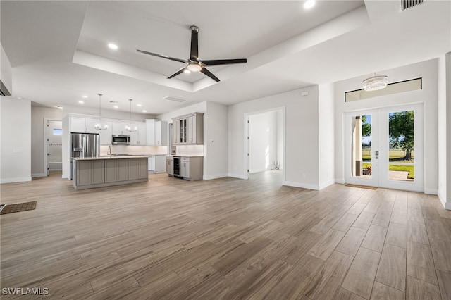 unfurnished living room featuring ceiling fan with notable chandelier, a tray ceiling, and sink