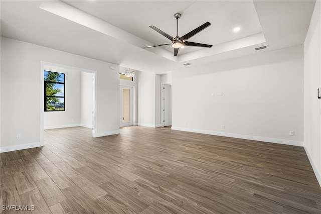 empty room with dark hardwood / wood-style floors, a raised ceiling, and ceiling fan