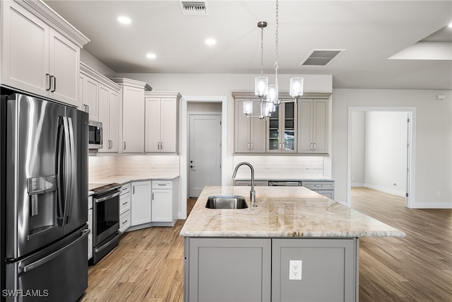 kitchen featuring sink, pendant lighting, appliances with stainless steel finishes, and a center island with sink