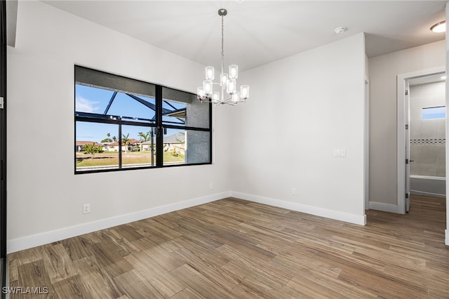 spare room with an inviting chandelier and wood-type flooring