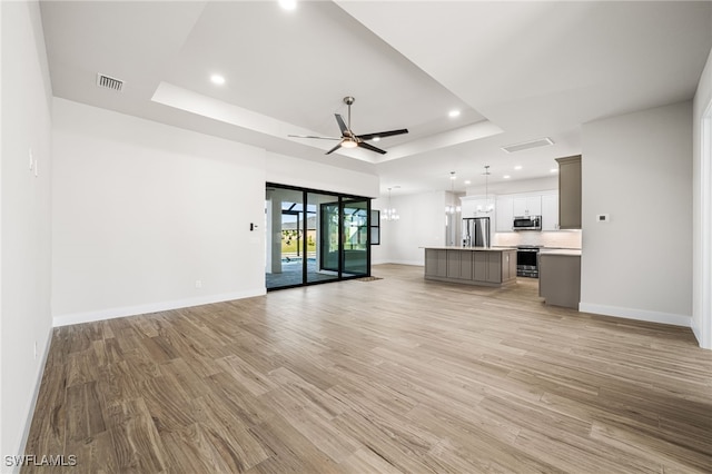 unfurnished living room featuring ceiling fan, light hardwood / wood-style floors, and a raised ceiling