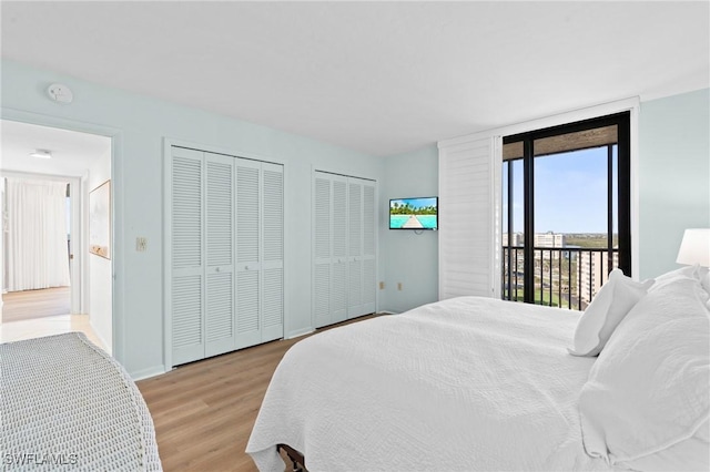 bedroom with baseboards, light wood-style flooring, access to exterior, floor to ceiling windows, and two closets