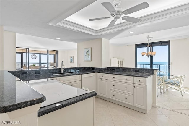 kitchen featuring a peninsula, a water view, a sink, white cabinetry, and a raised ceiling