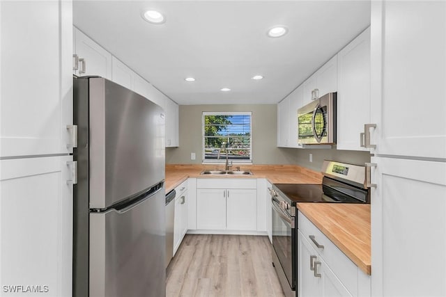 kitchen with sink, butcher block countertops, white cabinetry, light hardwood / wood-style flooring, and appliances with stainless steel finishes