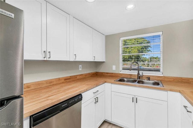 kitchen with appliances with stainless steel finishes, butcher block countertops, sink, and white cabinets