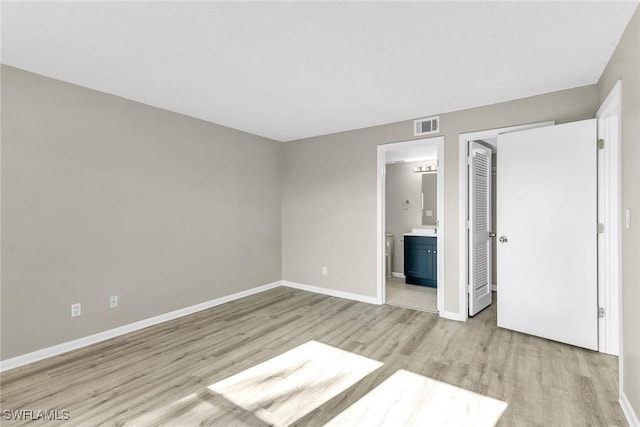 unfurnished bedroom featuring ensuite bathroom and light wood-type flooring