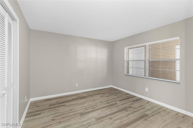 unfurnished room with a textured ceiling and light wood-type flooring