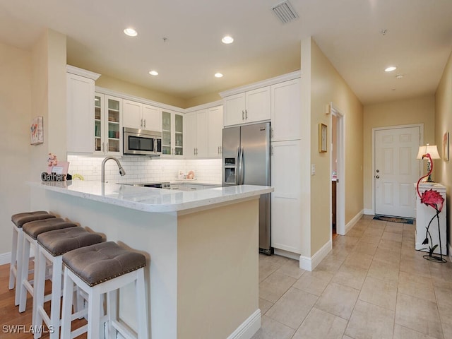 kitchen with white cabinetry, stainless steel appliances, tasteful backsplash, kitchen peninsula, and a breakfast bar area