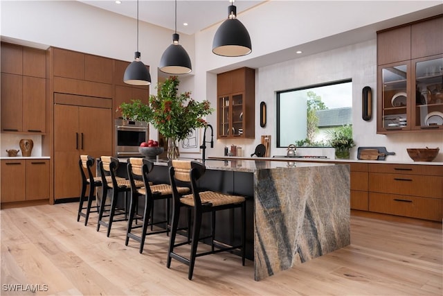 kitchen with stainless steel oven, light stone countertops, pendant lighting, paneled built in refrigerator, and light wood-type flooring