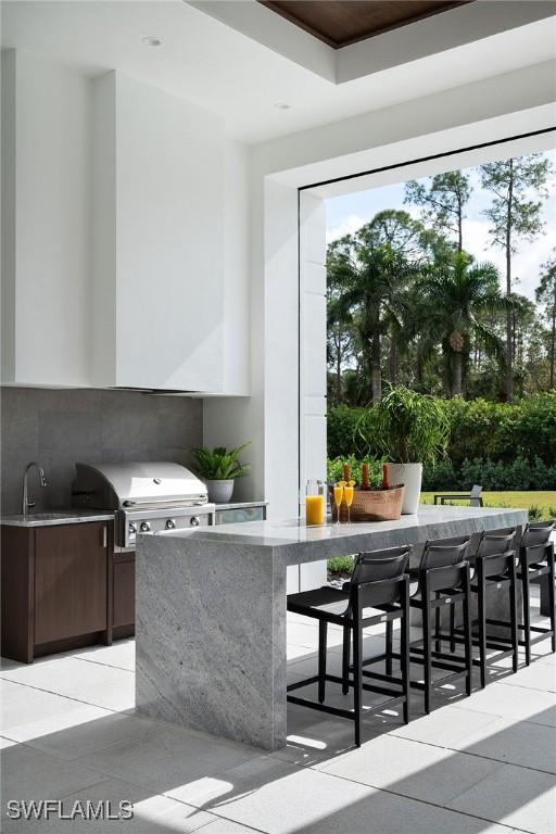 kitchen with a kitchen breakfast bar, light tile patterned floors, tasteful backsplash, dark brown cabinets, and sink