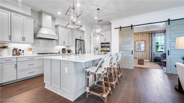 kitchen with custom range hood, a kitchen island with sink, a barn door, hanging light fixtures, and a breakfast bar area