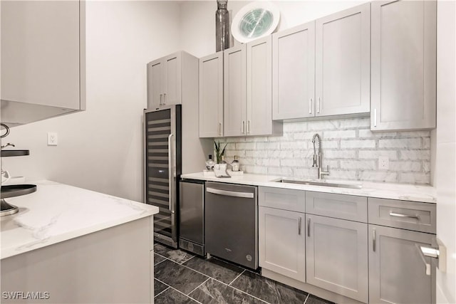 kitchen featuring sink, gray cabinetry, dishwasher, light stone countertops, and backsplash